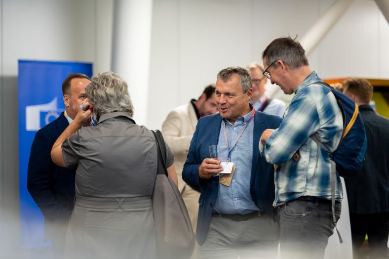 Gäste unterhalten sich beim Empfang im Foyer, ein Mann mit Namensband lacht