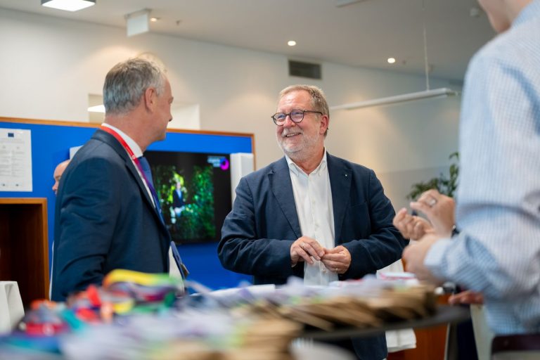 Zwei Männer im Sakko unterhalten sich lächelnd am Empfangstisch