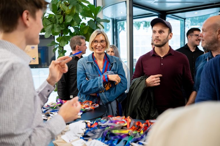 Gäste am Empfangstisch mit Namensbändern, eine Frau in Jeansjacke lächelt