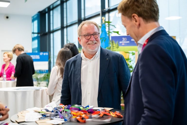 Grauhaariger Mann mit Brille lacht im Gespräch neben dem Empfangstisch