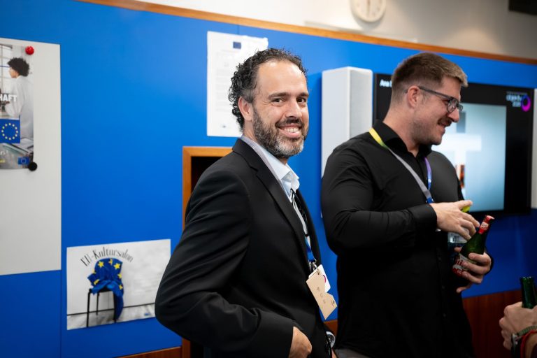 Zwei Männer lachen im Gespräch vor einer blauen Wand