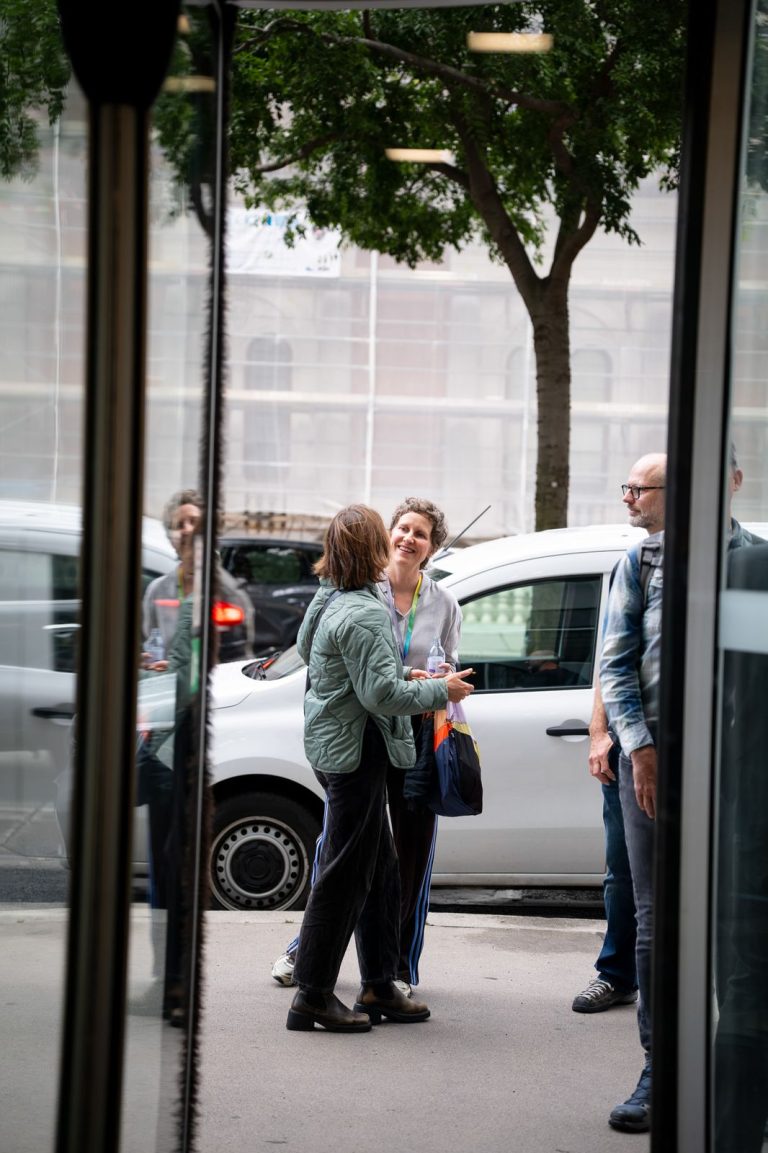 Blick durch die Glastür auf Gäste, die vor dem Gebäude auf dem Gehsteig plaudern