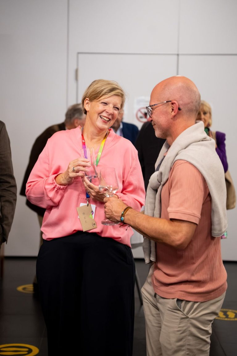 Frau in rosa Bluse und Mann in lachsfarbenem Hemd lachen im Gespräch