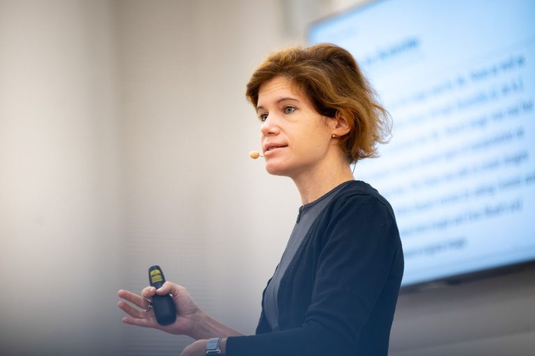 Vortragende mit Presenter vor einer Projektion mit Text