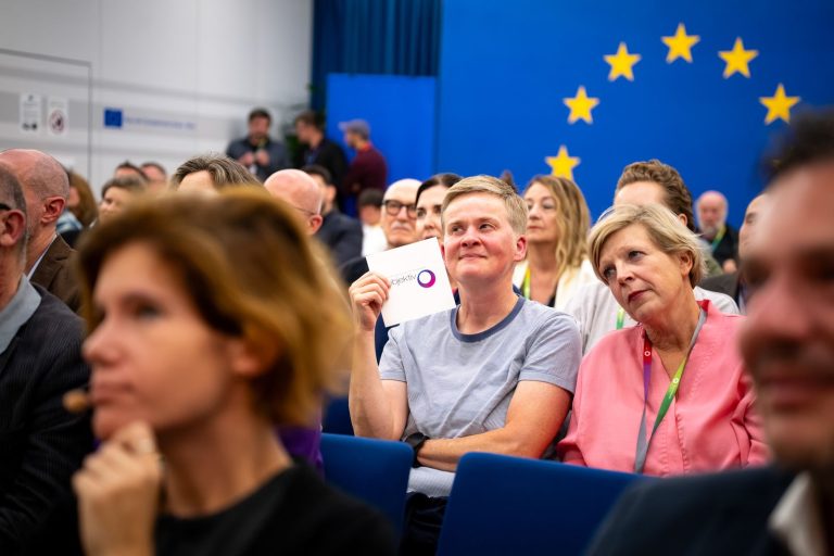 Publikum vor dem EU-Sternenkreis, eine Frau hält eine Karte hoch