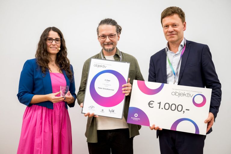Preisübergabe Kultur, 3. Platz: Peter Gründhammer mit Urkunde, daneben die Moderatorin mit Trophäe und ein Mann mit Scheck über 1.000 Euro
