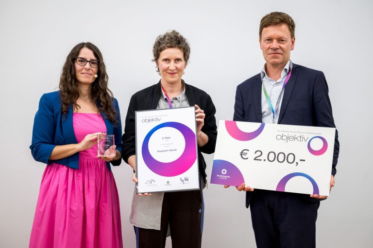 Preisübergabe Kultur, 2. Platz: Elisabeth Mandl mit Urkunde, daneben die Moderatorin mit Trophäe und ein Mann mit Scheck über 2.000 Euro