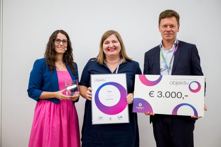 Preisübergabe Kultur, 1. Platz: Luiza Puiu mit Urkunde, daneben die Moderatorin mit Trophäe und ein Mann mit Scheck über 3.000 Euro