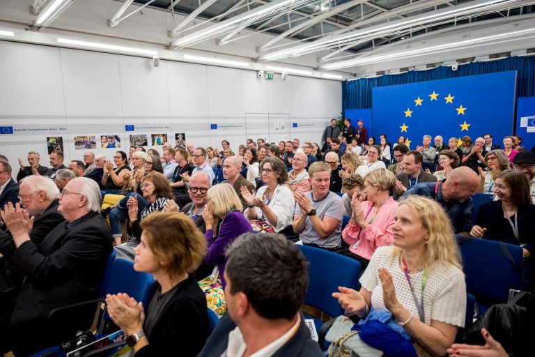 Publikum applaudiert im Saal mit dem EU-Sternenkreis