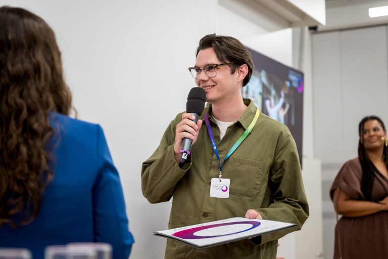 Preisträger mit Brille spricht ins Mikrofon, im Hintergrund die Moderatorin