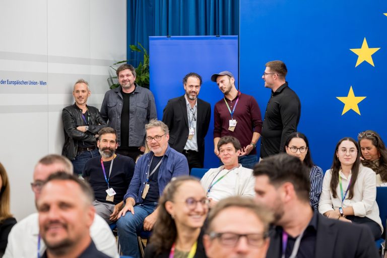 Gäste sitzen und stehen vor der blauen Wand mit EU-Sternen
