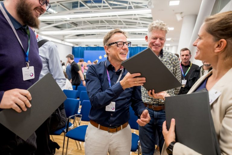 Preisträger mit Urkundenmappen gratulieren einander nach der Verleihung