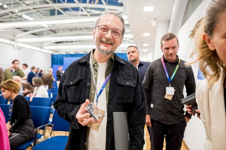 Mann mit Bart hält lachend eine gläserne Trophäe