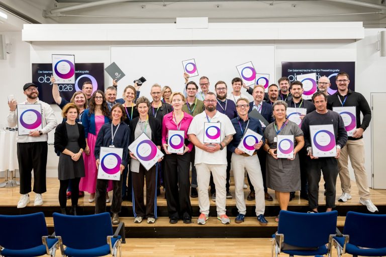 Gruppenfoto der Preisträger:innen und Nominierten mit ihren Urkunden vor den Objektiv-Bildschirmen