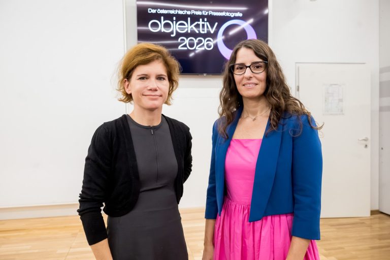 Vortragende und Moderatorin posieren vor dem Bildschirm mit dem Logo „objektiv 2026“