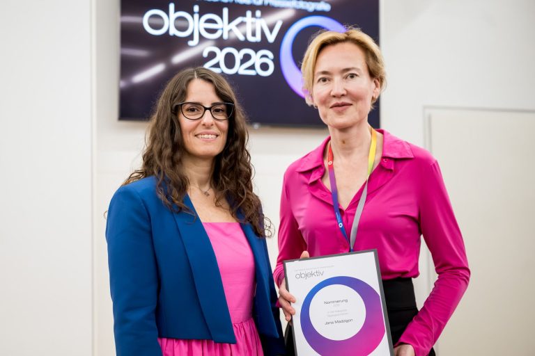 Die Moderatorin und Jana Madzigon mit ihrer Nominierungsurkunde in der Kategorie Tagesgeschehen vor dem Objektiv-Logo