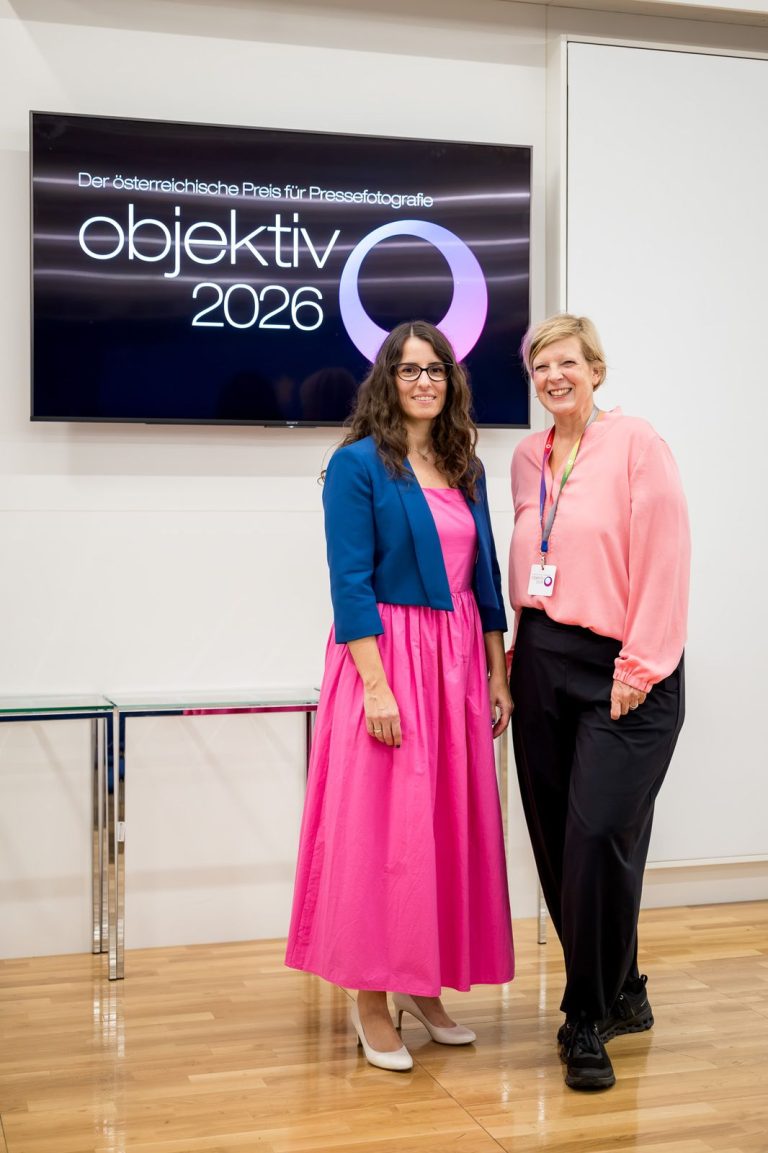 Moderatorin und eine Frau in rosa Bluse posieren vor dem Objektiv-Logo