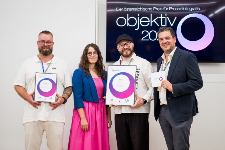Preisträger mit Urkunden und die Moderatorin posieren vor dem Objektiv-Logo