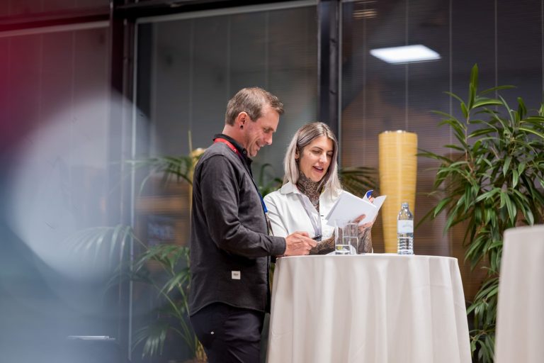 Mann und Frau blättern an einem Stehtisch in einer Broschüre