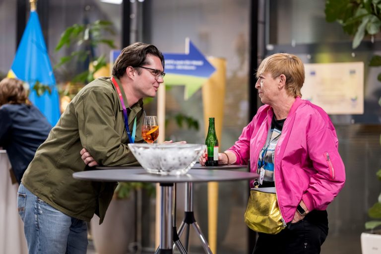 Mann und Frau in pinker Jacke plaudern an einem Stehtisch